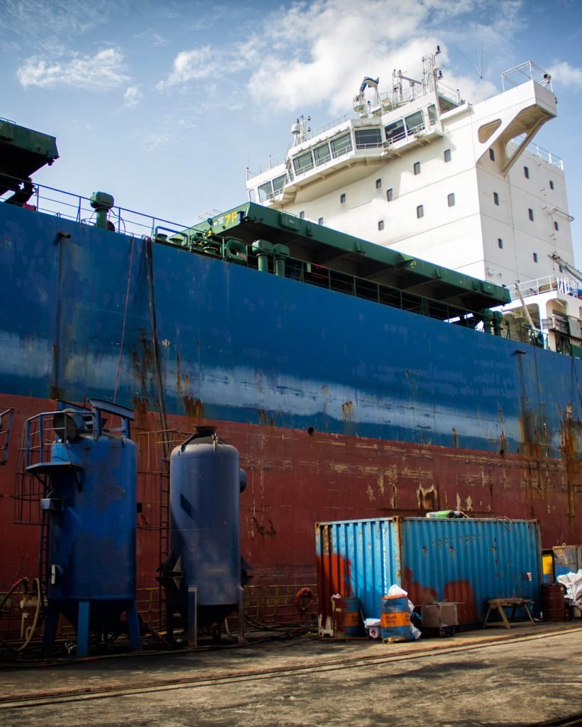 A large tanker cargo ship is being renovated and painted in shipyard dry dock
